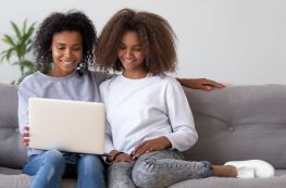 Happy African Mother And Teen Daughter Using Laptop On Sofa